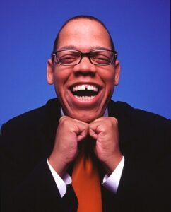 Greg Morton smiling widely with chin resting on closed hands promotional