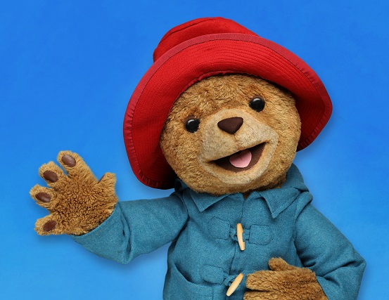 Paddington the Bear infron of blue background waving, wearing red hat