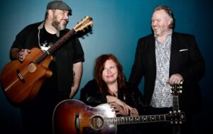 A'Court, Spiegel & Vinnick together holding instruments in front of blue background