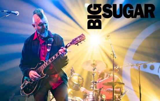 Gordie Johnson on stage playing guitar. Big Sugar Logo on side