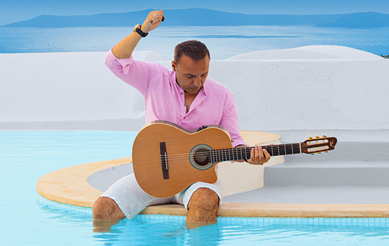 Pavlo sitting at the edge of the pool, legs in the water. He is playing a guitar.